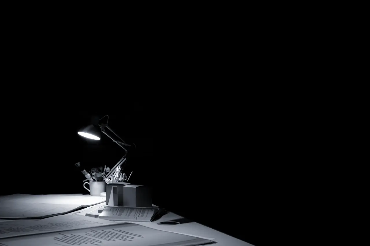 A desk lamp lighting papers in a dark room